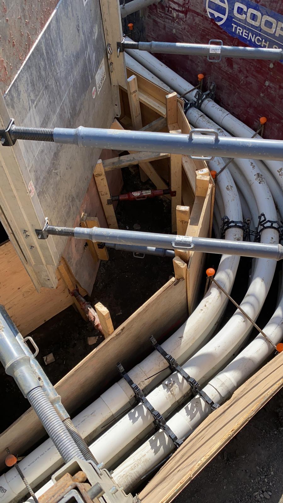 Multi-duct PVC conduit bank installed inside shored trench with hydraulic struts