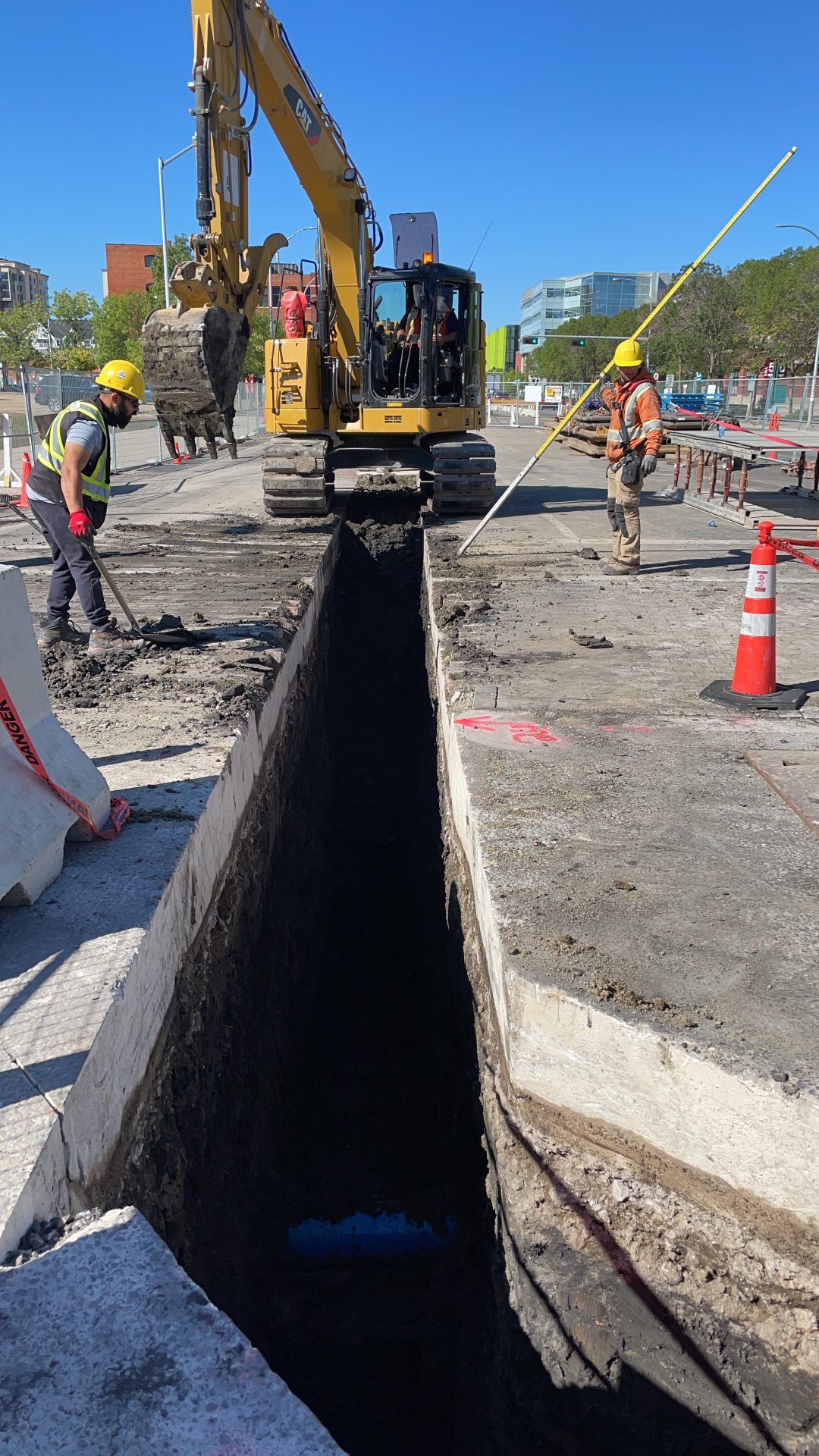ASI Tech CAT excavator trenching downtown street with crew and traffic control