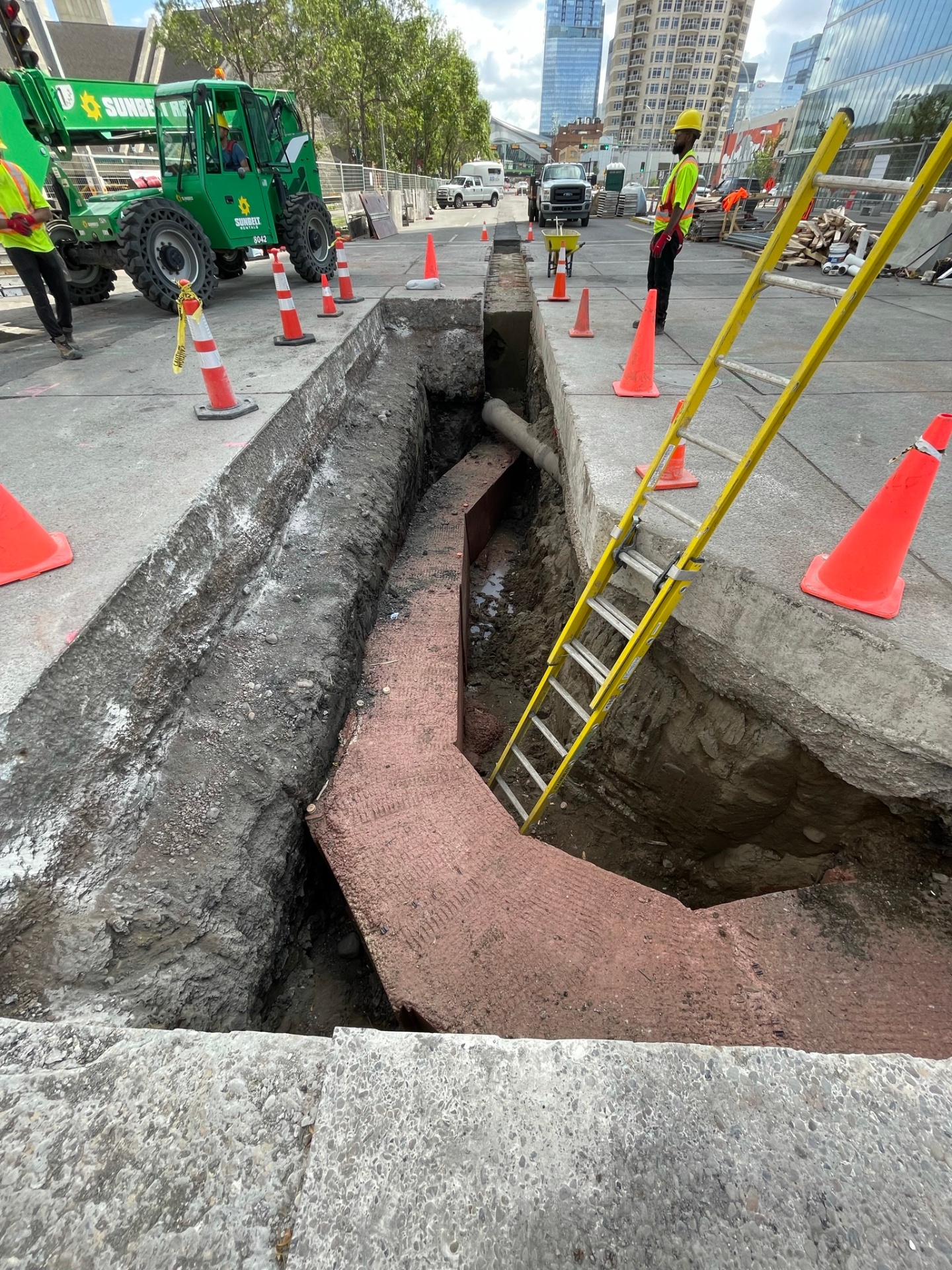 Deep shored excavation with red shoring plates and access ladder in downtown core