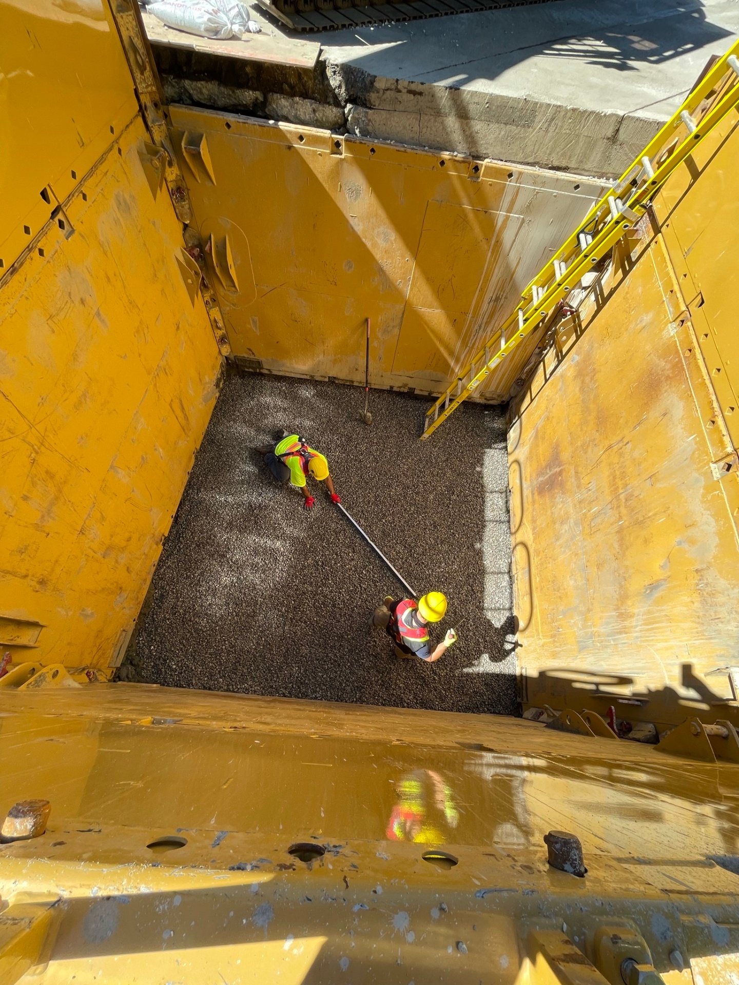 Crew screeding gravel bedding inside large yellow trench shoring box