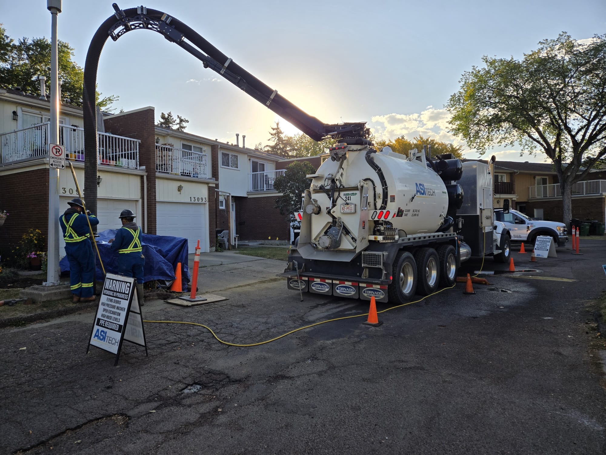 ASI Tech hydrovac truck with extended boom on residential street at sunset